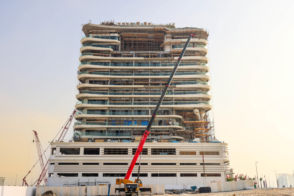 Beach Walk Residence Construction of a modern multi-story building with scaffolding and cranes in the foreground against a clear sky.
